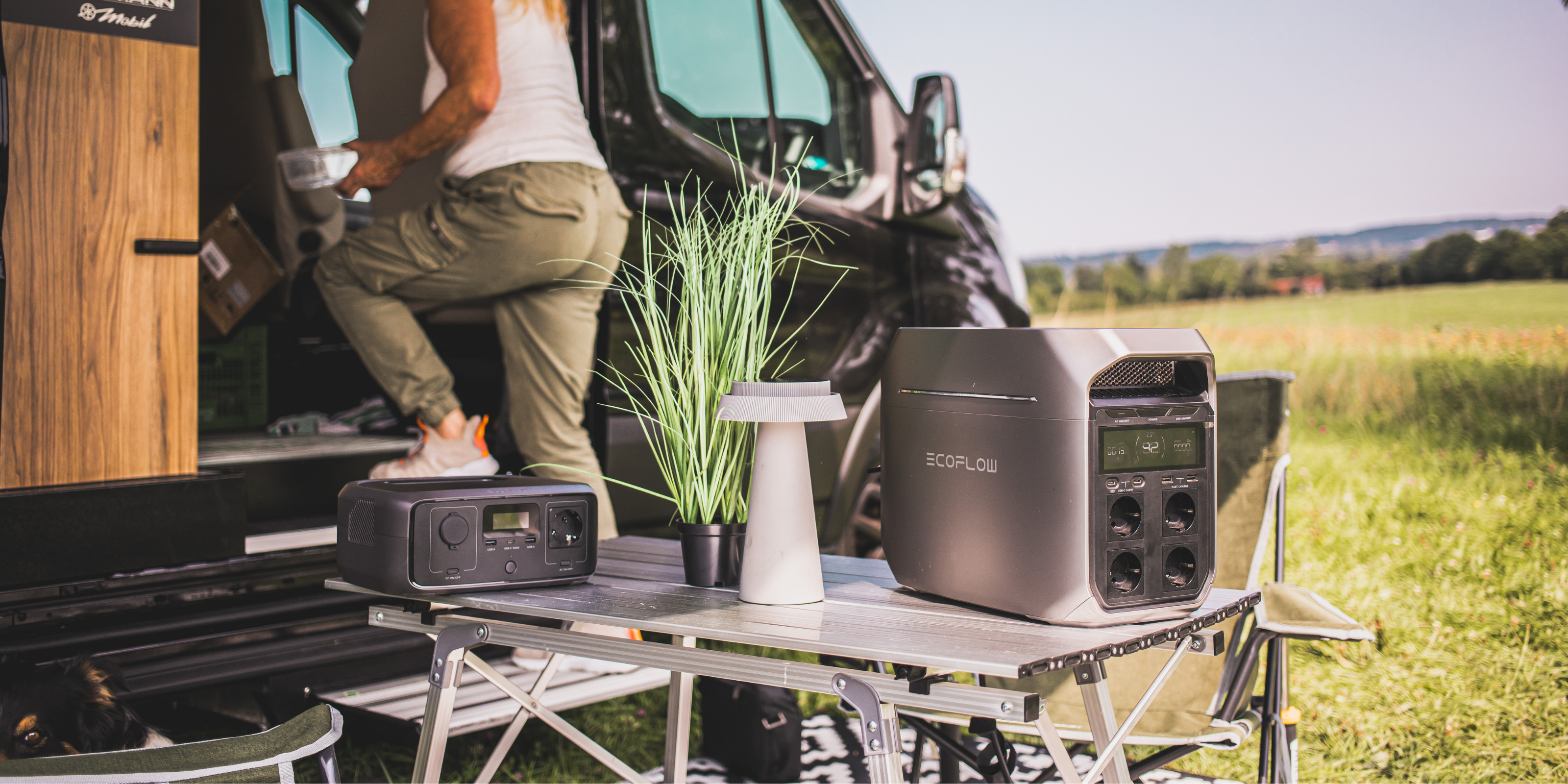 Vor einem Camper steht ein Tisch auf dem zwei Powerstations von EcoFlow stehen. Eine Frau steigt gerade in das Fahrzeug ein.